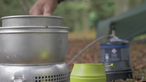 Preparing-two-hot-beverages-in-the-forest-while-camping,-Static-Shot