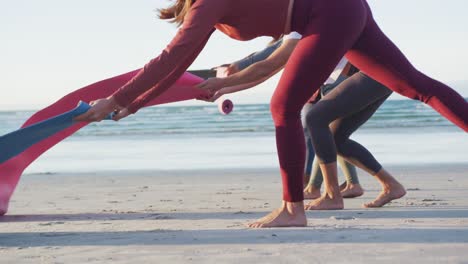 Group-of-diverse-female-friends-preparing-yoga-mats-before-practicing-yoga-at-the-beach