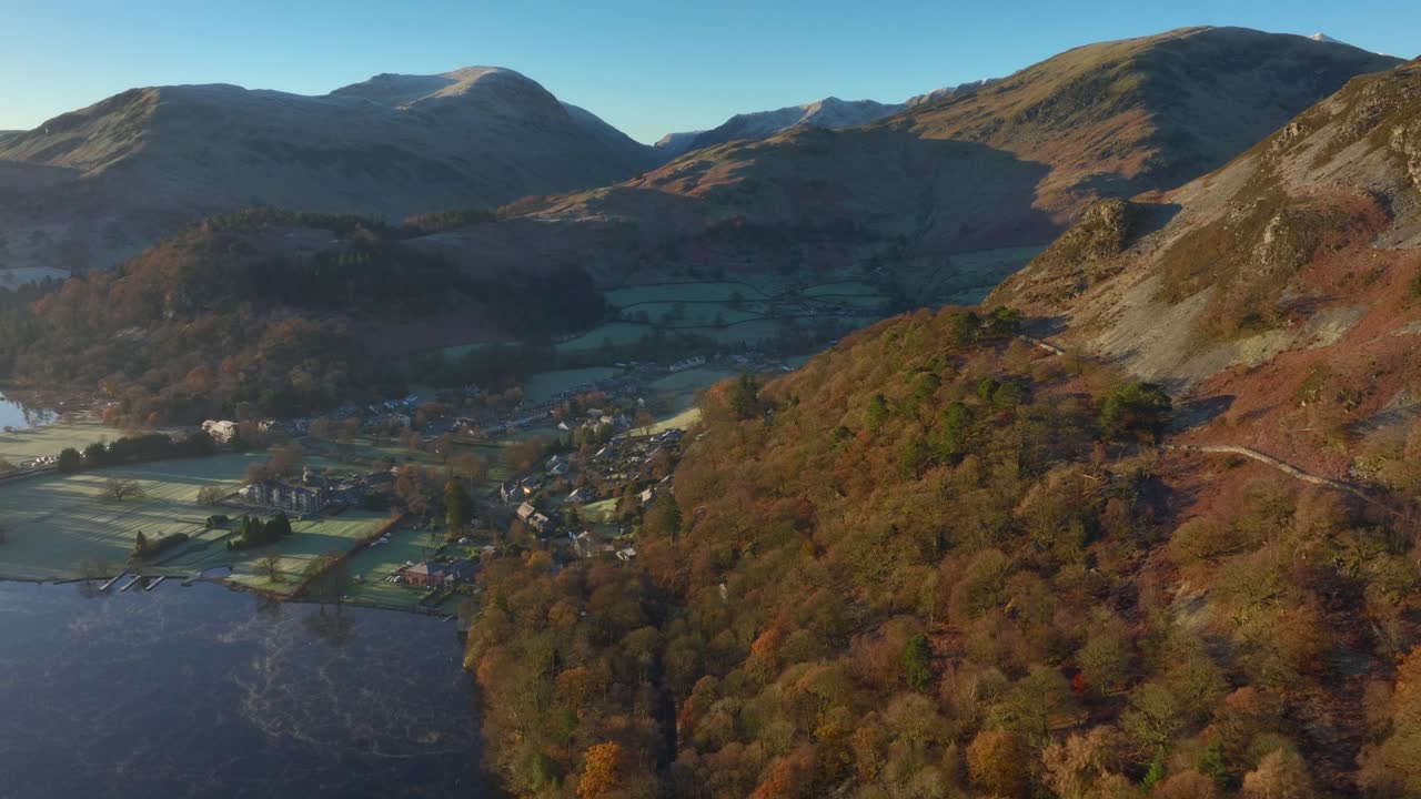 amanecer de otoño sol en los árboles de la ladera con la ciudad de la orilla del lago respaldada por las montañas