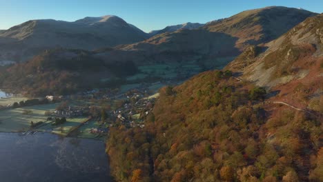 autumn sunrise sunshine on hillside trees with lakeside town backed by mountains
