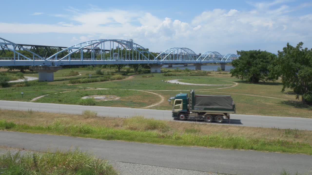 Dump Truck Driving In The Road Within Yodogawa Riverside National Park With Aqueduct Bridge In Osaka, Japan. - wide shot