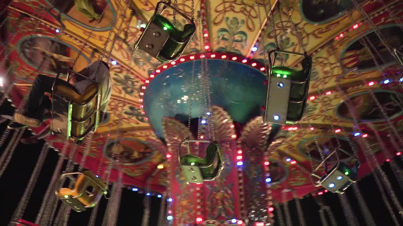 Father and daughter having fun in a colorful carousel at night in a park in slow motion