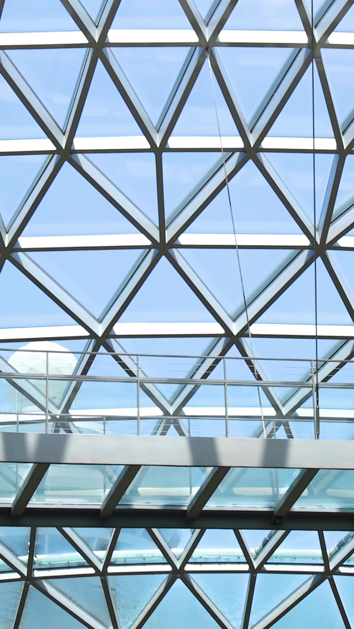 Camera tilts from misty indoor waterfall to reveal glass dome ceiling and daylight-filled atrium.