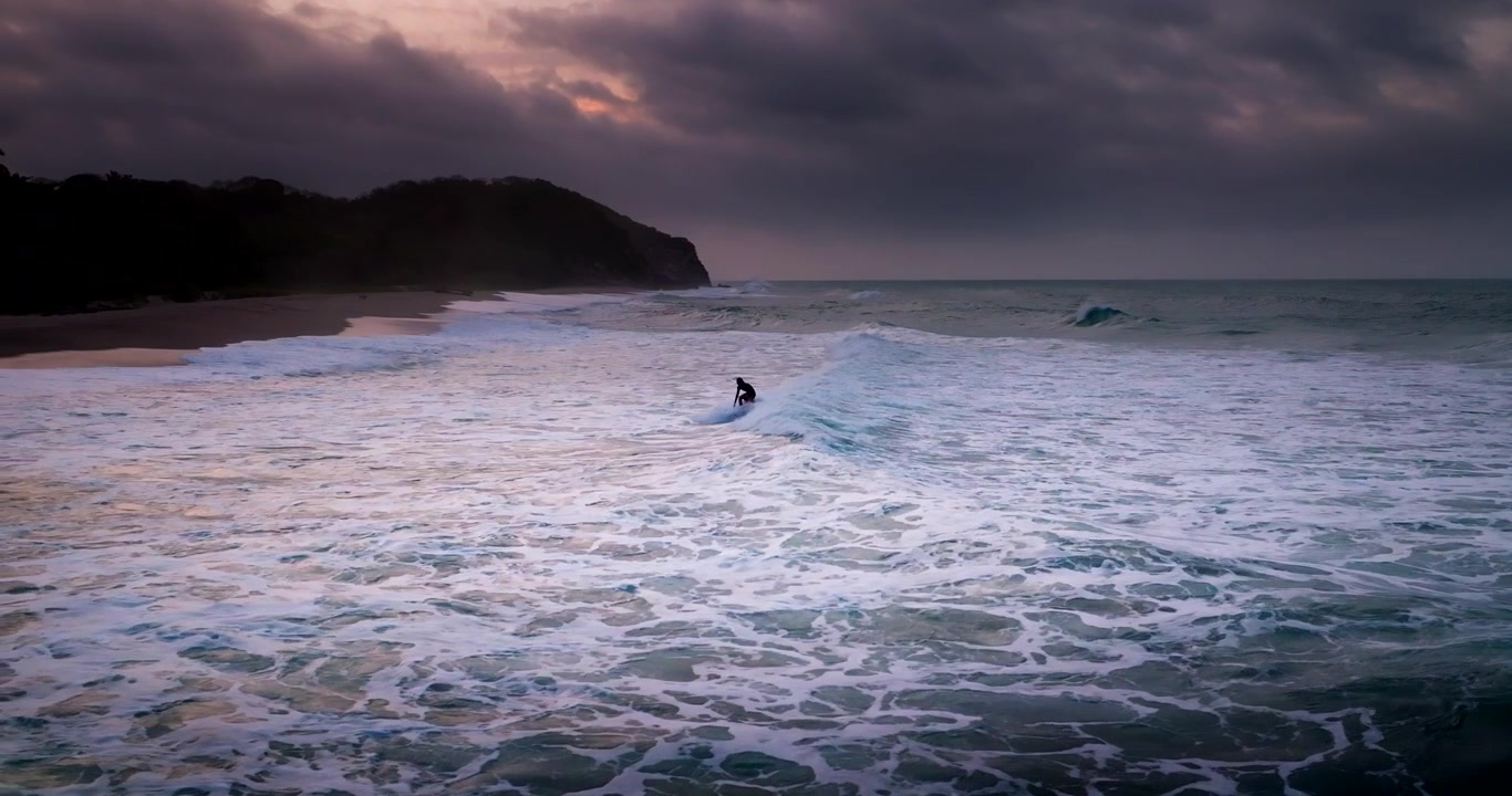 Surfista su un'onda che si dirige verso la spiaggia al tramonto a Tayrona Los Naranjos, ripresa aerea al rallentatore