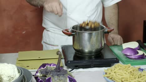 chef dips grated metal skimmer into pot and pulls out fried eggplant cubes from oil