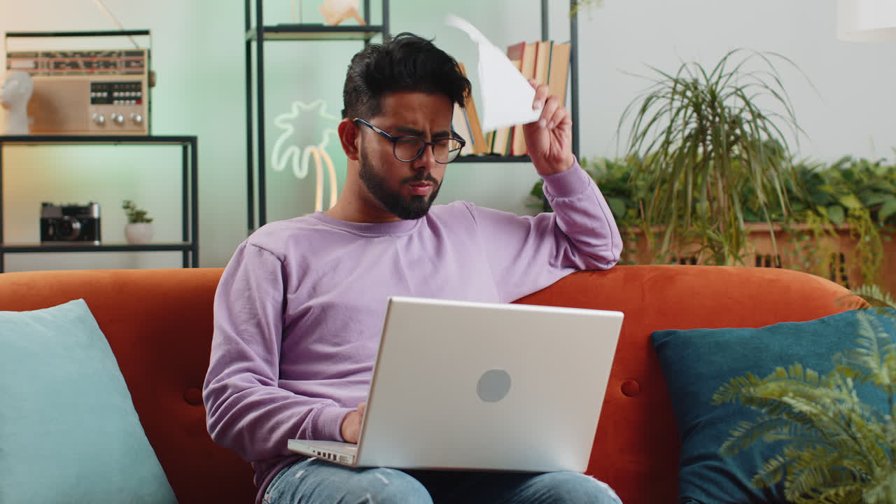 Stressed indian man looking at unpaid bank debt loan doing paperwork planning budget throws bills