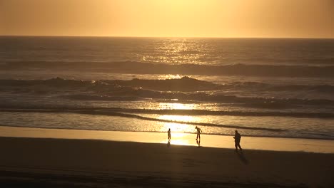 A-Man-And-Two-Children-Play-Along-The-Water'S-Edge-In-The-Goldenhour