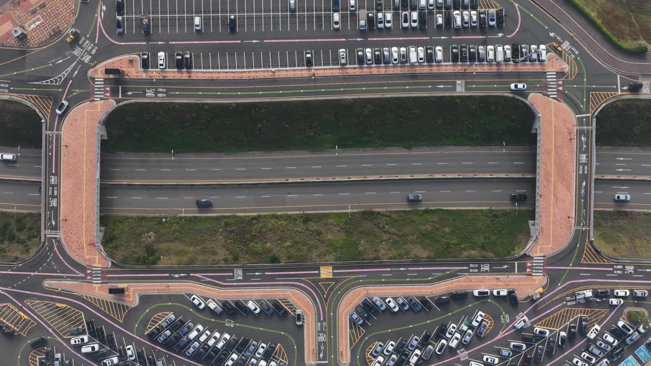 Cars driving between tightly packed parking spaces on either side of the highway.