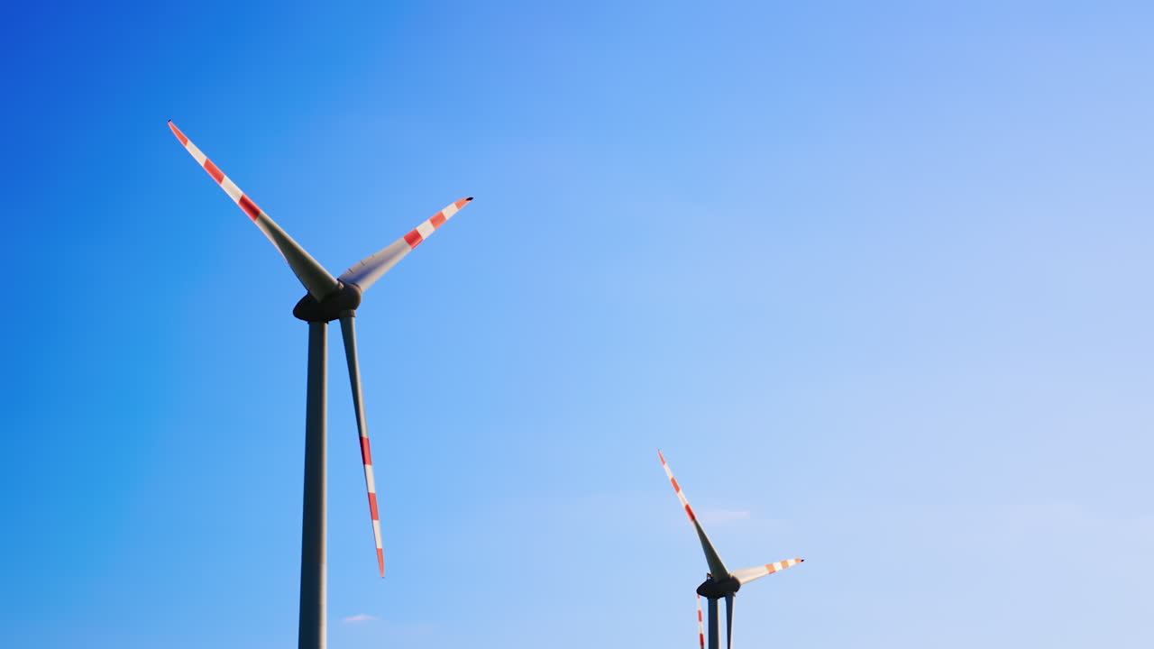Turbines rise blue sky high. Two wind turbines with red and white stripes spin under a clear blue sky, showcasing renewable energy in action