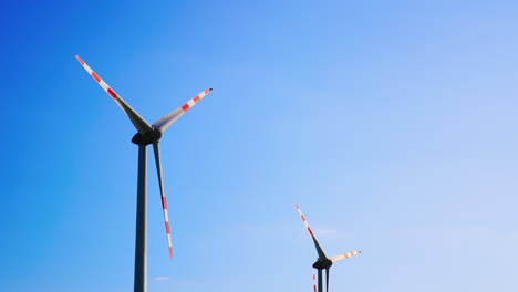 turbines rise blue sky high. two wind turbines with red and white stripes spin under a clear blue sky, showcasing renewable energy in action