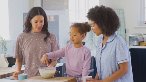 Familie-Mit-Zwei-Müttern-Im-Schlafanzug,-Die-Zu-Hause-Mit-Ihrer-Tochter-Morgenpfannkuchen-In-Der-Küche-Backen