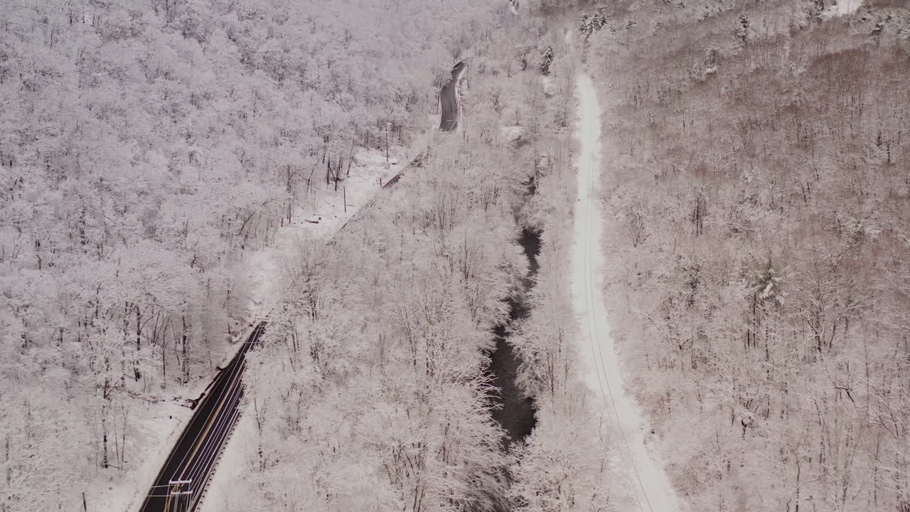 Aerial of a mountain highway river and railroad tracks covered in snow with vehicles driving