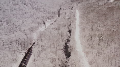 aerial of a mountain highway river and railroad tracks covered in snow with vehicles driving