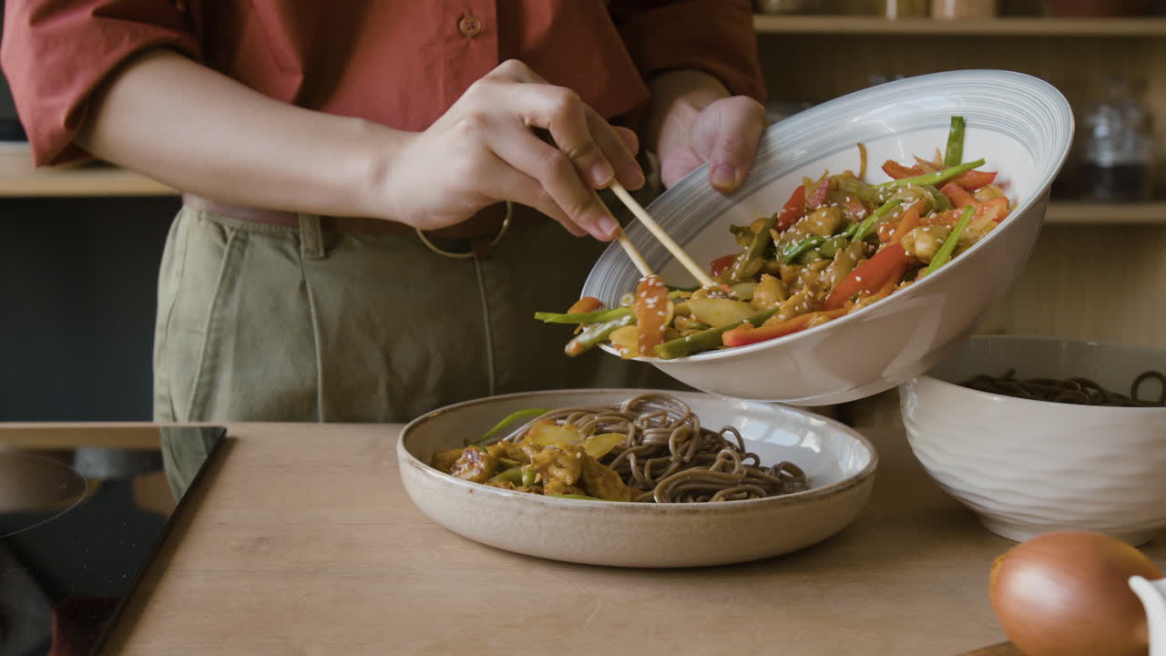 A person serving stir-fry with noodles in a kitchen