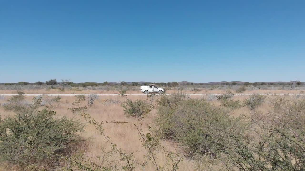 나무 뒤에 있는 단일 색 4x4 밴 지프 오프로드 차량의 드론 항공 비디오 영상. 색 지프에서 멀리 떨어진 쪽으로 나무를 날아가는 드론. 자동차와 자연의 흥미로운 시각 각도.