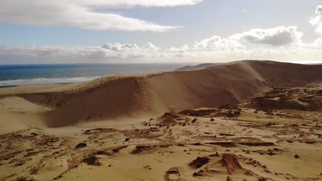 aerial descent to sand dune, ocean and white cloudy sky in background