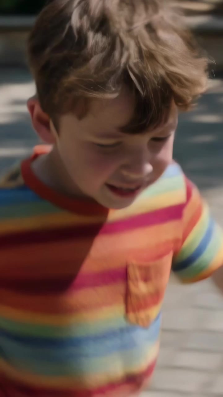 Video verticale: La telecamera inizia a seguire un bambino che corre con una maglietta arcobaleno, ridendo sui sampietrini.