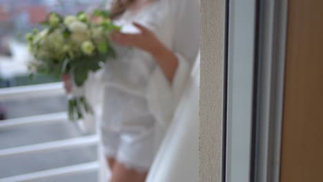bride holding bouquet in soft white robe on balcony with city view in background