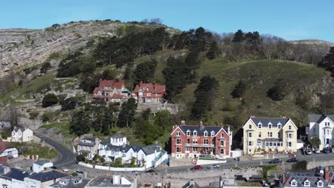 Colourful-Llandudno-seaside-holiday-town-hotels-against-Great-Orme-mountain-aerial-view-orbit-left-pan-right