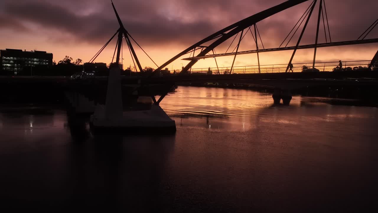 Static drone shot of South Bank's Goodwill Bridge at sunrise, with bridge silhouetted over orange sky