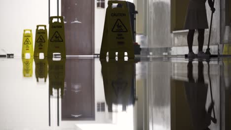 sirvienta limpiando piso brillante con múltiples señales de precaución
