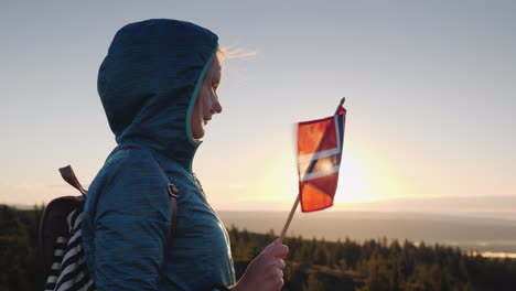 a traveler with the flag of norway in his hand meets the sunrise on the top of the mountain enjoys t