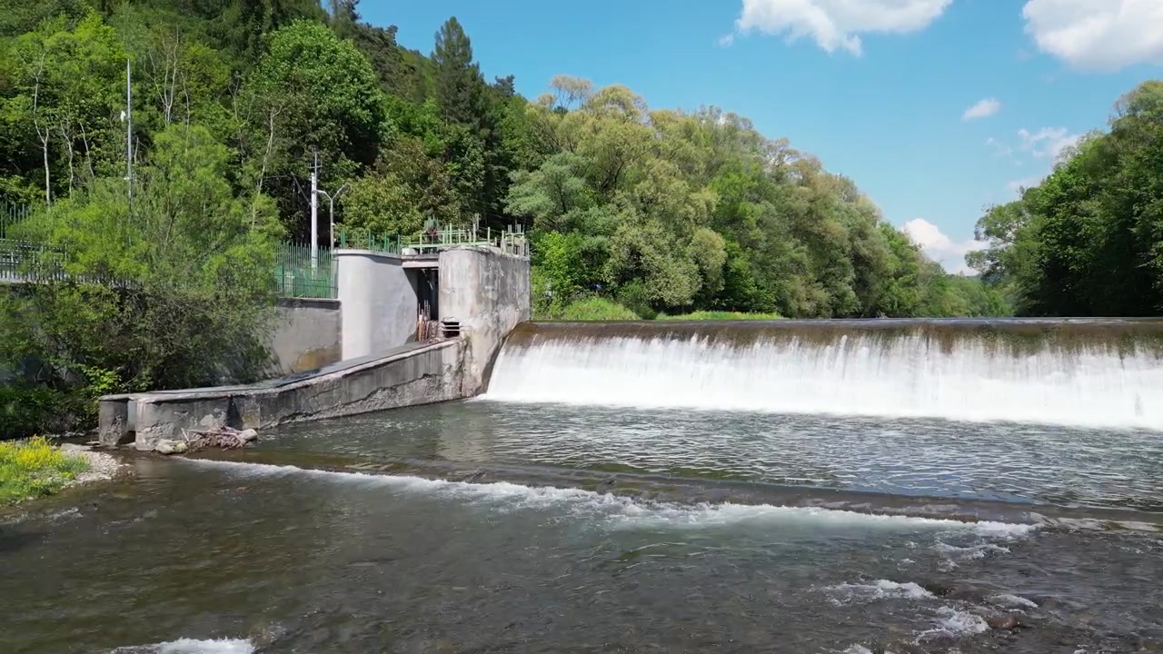 Paesaggio estivo aereo che mostra il fiume Koszarawa, acqua che scorre su uno sbarramento, strutture idrotecniche, riva rocciosa, vegetazione lussureggiante e un ambiente naturale tranquillo