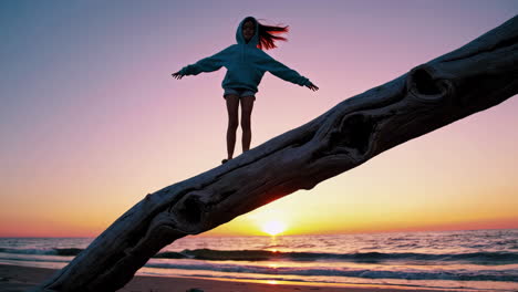 girl balancing on driftwood at sunset beach