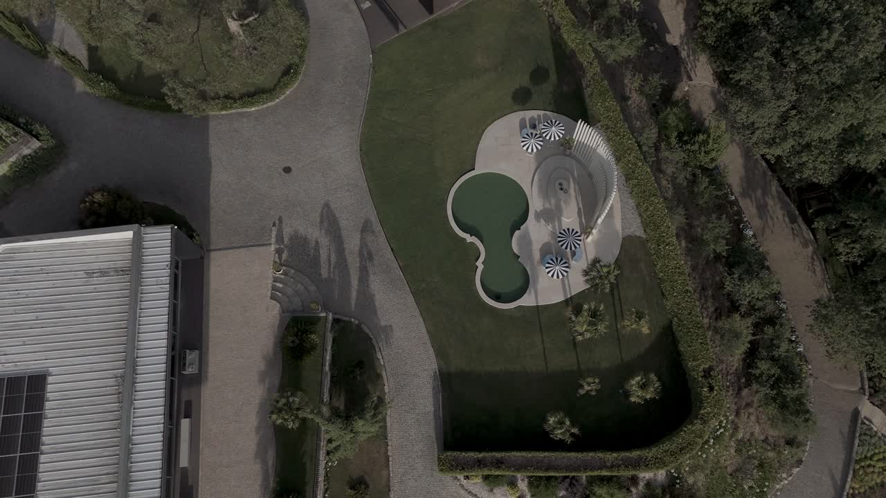 aerial - uniquely shaped pool with striped parasols in a landscaped garden with modern paving