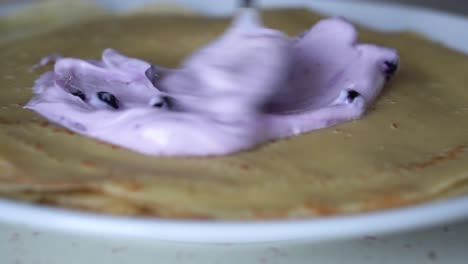 vista de cerca de la crema de arándanos púrpura que se extiende sobre un panqueque francés en un plato blanco