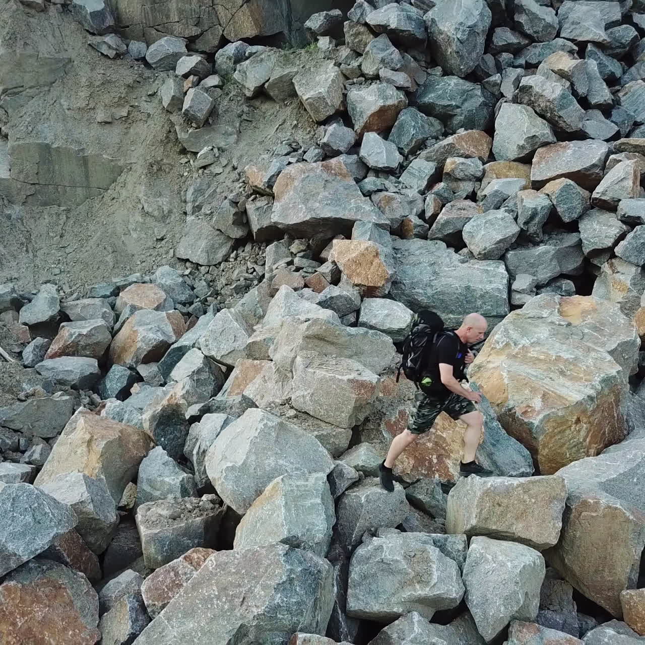 Hiker man in shorts and black t-shirt with a big rucksack climbing down the stones. Panoramic view of rocky landscape and a traveller walking down.
