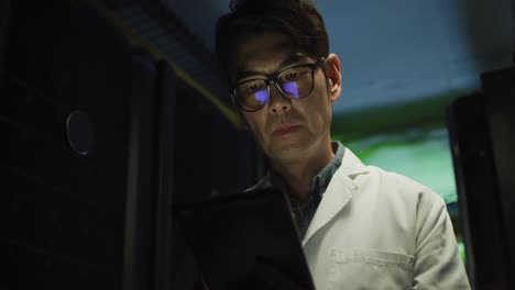 Asian-male-it-technician-in-lab-coat-using-tablet-checking-computer-server