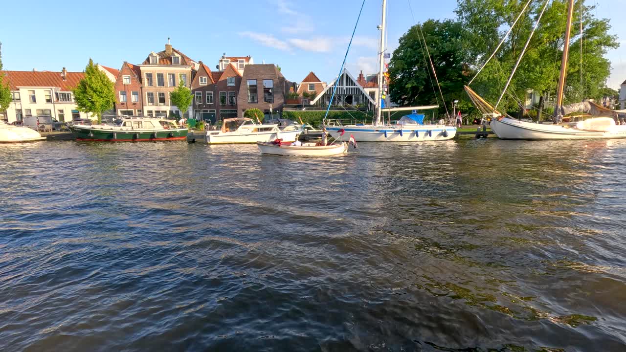 Small boats travel on canal with historic Dutch buildings, bright daylight, and gentle camera movement