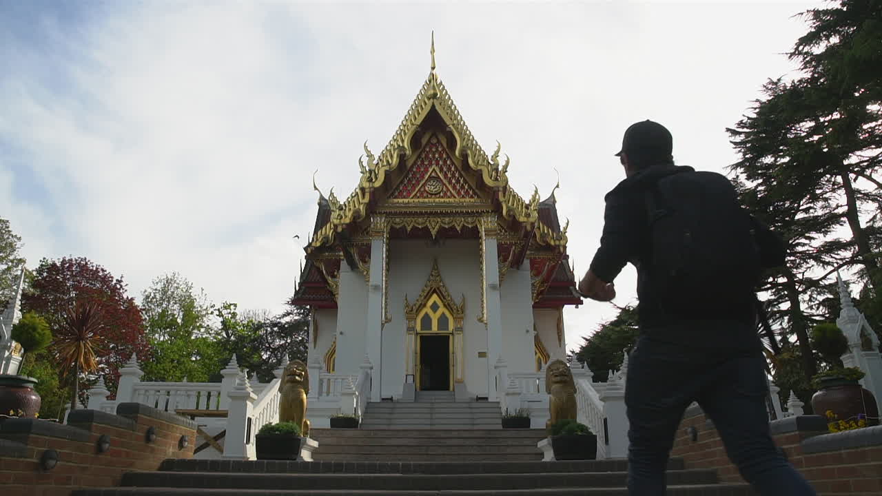 Slow Motion of a tourist man arriving at a Thai Buddhist Temple at sunset time and looking in the distance with birds flying