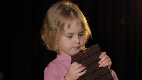 niño atractivo comiendo un enorme bloque de chocolate. chica rubia linda