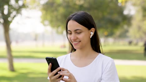 Mujer-India-Poniéndose-Auriculares-En-Los-Oídos-Antes-De-Hacer-Ejercicio-Y-Correr-En-Un-Parque-Por-La-Mañana