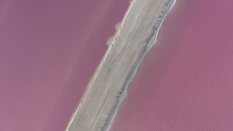 sandy causeway between salt evaporation ponds gone pink with algae