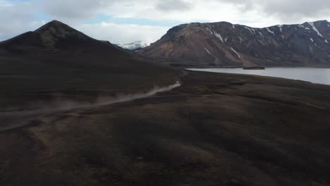 Majestätischer-Hochwinkelblick-Auf-Den-Skaftafell-nationalpark-Mit-Schneebergen-Und-Gletschersee-In-Island.-Vogelperspektive-Von-Offroad-Autos,-Die-Eine-Unbefestigte-Straße-Fahren,-Die-Staubwolken-Aufwirbelt.-Wildnis-Und-Abenteuer