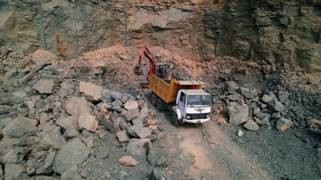 Aerial zoom in drone shot of excavator loading rocks and soil on the truck in India
