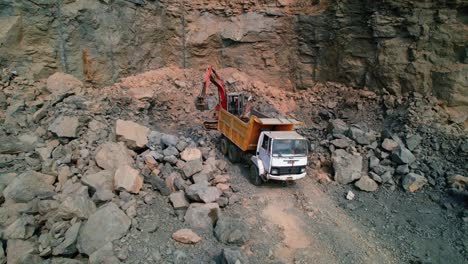 aerial zoom in drone shot of excavator loading rocks and soil on the truck in india