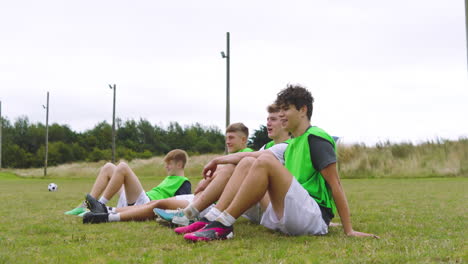 male soccer players sitting in row and observing game and clapping hands on pitch