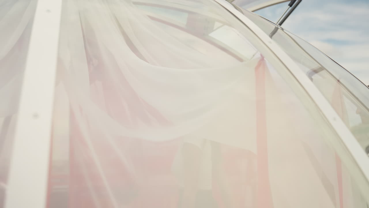 rooftop couple caucasian inside glass dome sharing tender summer moment with sheer pink drapes, city skyline in background, soft sunlight filtering through translucent canopy as man leads woman into