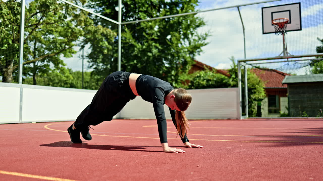 Young woman doing high-intensity exercises on an outdoor sports ground. Athlete pulling her legs up to her chest from a push-up position. Workout, fitness, outdoor exercises to strengthen the body