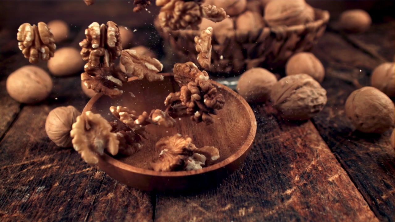Gherigli di noce che cadono in una ciotola di legno su un tavolo rustico.