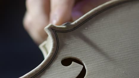 Close-up view shows a luthier precisely carving violin edge near purfling channel and elegant f-hole curve on a spruce violin, highlighting craftsmanship, tradition, wood grain, and accuracy