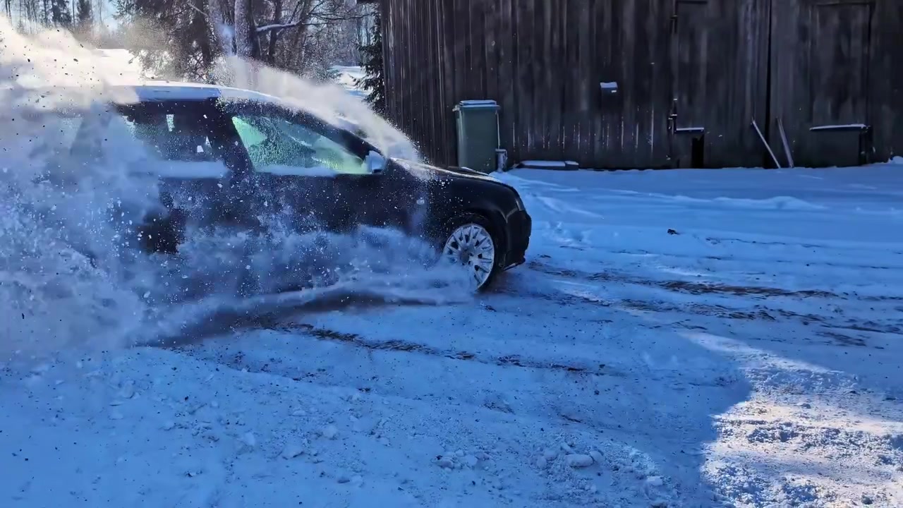 Slowmotion af en kraftfuld bil, der drifter på en glat vej og sprøjter sne mod kameraet.