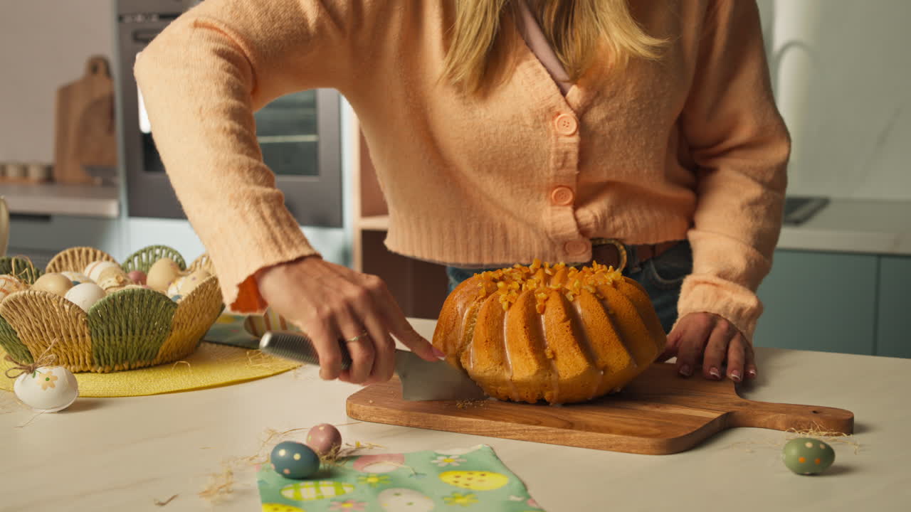 Hands slicing glazed Easter bundt cake on kitchen counter with festive decorations