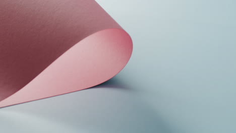 Close-up-of-pink-rolled-piece-of-paper-on-pale-blue-background-with-copy-space-in-slow-motion