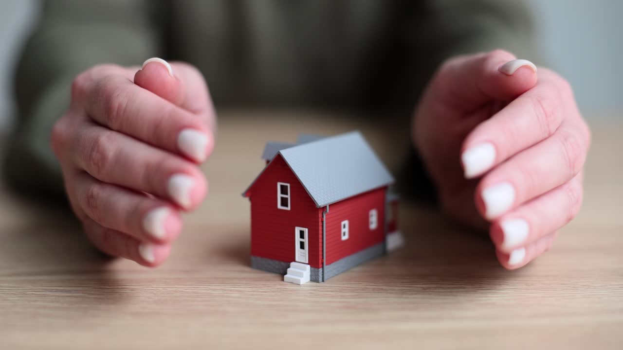 Hands protecting a miniature red house, symbolizing home security or property insurance