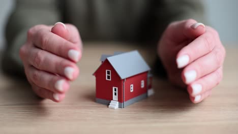 hands protecting a miniature red house, symbolizing home security or property insurance